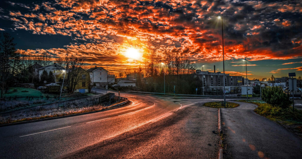 Serene Evening Skies: Captivating Sunset Casting a Warm Glow on a Charming Town with Lush Trees and Cozy Houses Wallpaper