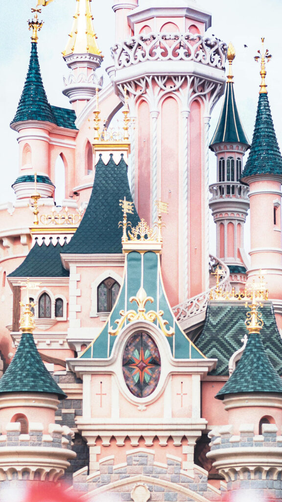 Disneyland Castle wallpaper with pastel pink walls and ornate green rooftops in fairy-tale style