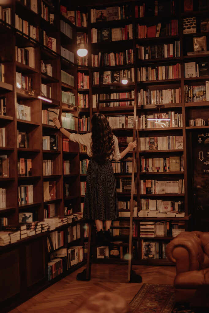 Woman on library ladder among towering bookshelves warm cozy book lover wallpaper background