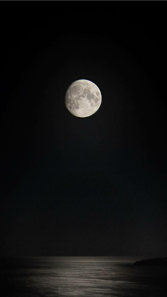 Enchanting Lunar Glow: iPhone Wallpaper showcasing a mesmerizing full moon amidst a captivating dark backdrop
