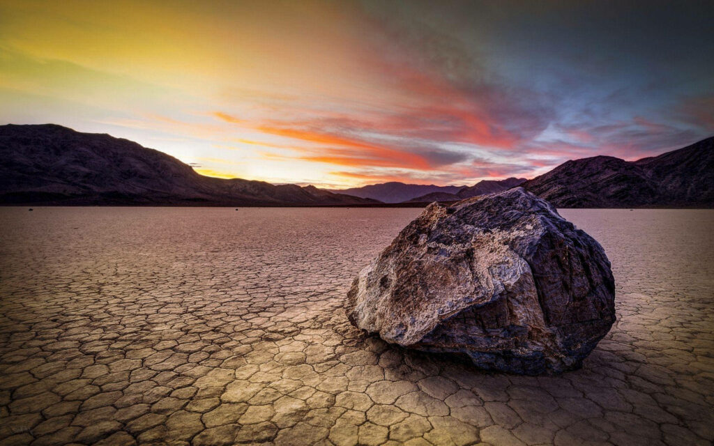 Mysterious Sailing Stones Bathed in Orange Sunset: Death Valley's Mesmerizing Landscape Wallpaper