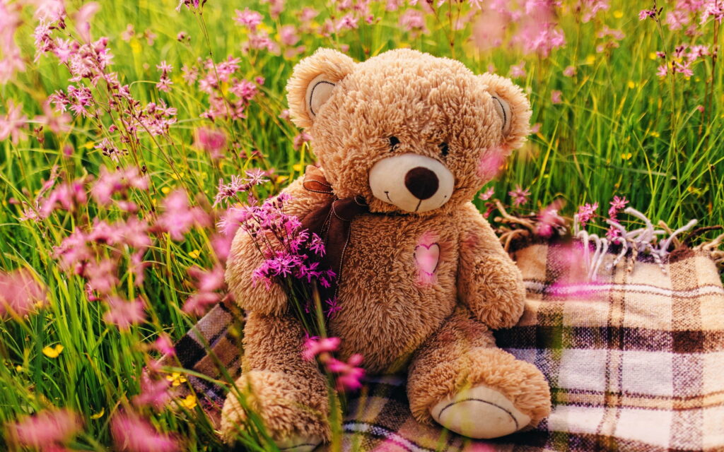 Whimsical Delight: A Teddy Bear Basking Amongst Vibrant Purple Blooms Wallpaper