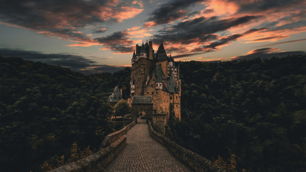 Majestic Eltz Castle at sunset with fiery sky and lush forest HD wallpaper background