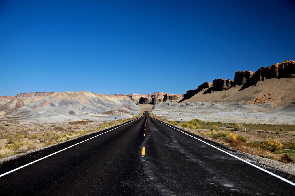 Long empty desert road through towering canyon rocks under bright vivid blue sky wallpaper background