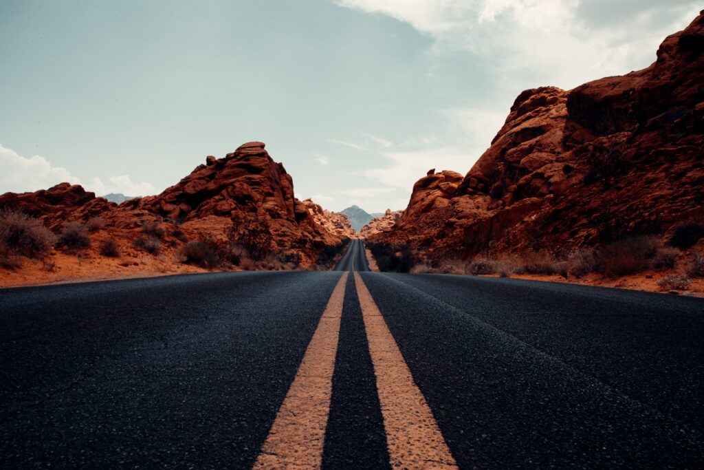 Straight desert road with yellow lines flanked by red rocks under bright blue sky wallpaper