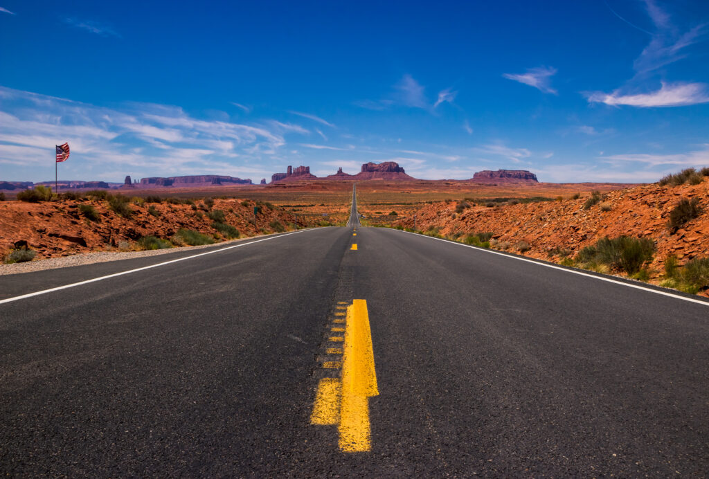 Straight asphalt road through desert valley with sandstone monuments under vivid blue sky Wallpaper