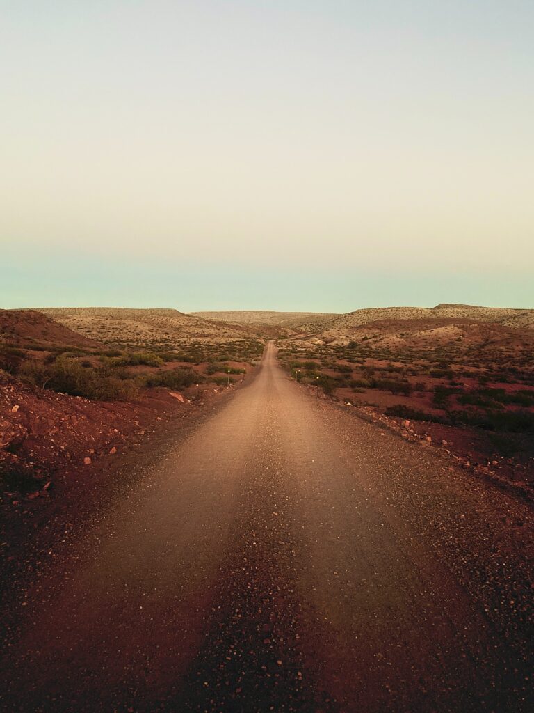 Long empty desert road with rocky hills and pastel sky evokes solitude and adventure wallpaper