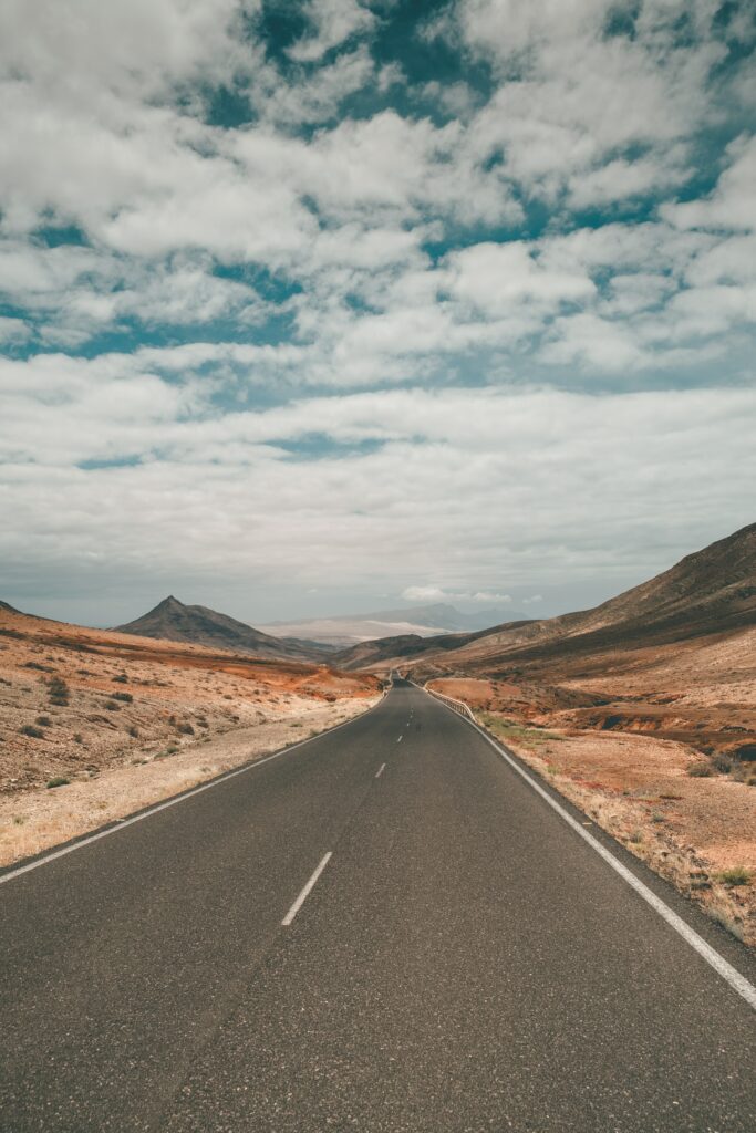 Long empty road through vast desert and rugged mountains under a bright blue sky wallpaper background