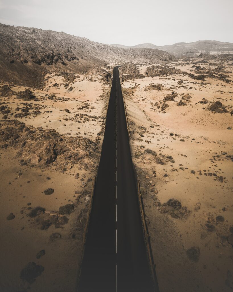 Long straight desert road with white markings mountains in distance barren landscape wallpaper