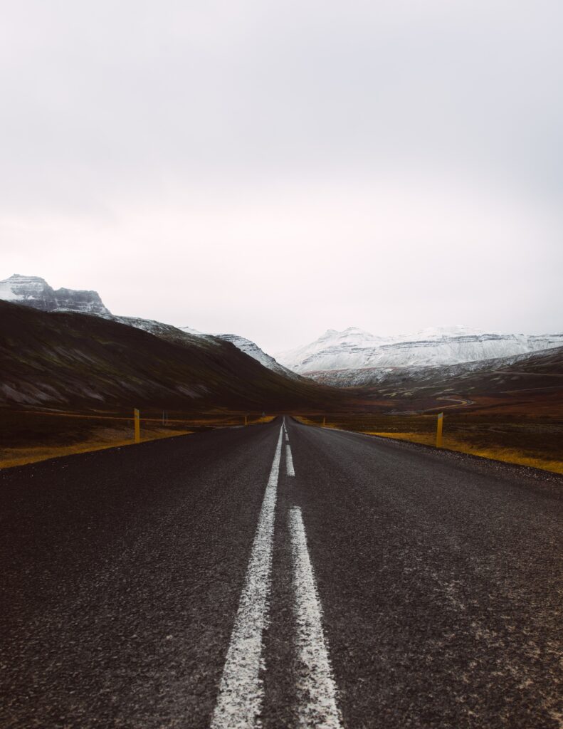 Straight road with white markings leading toward snow-capped mountains under cloudy sky wallpaper background