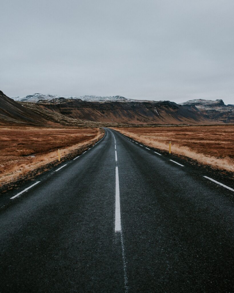 Long empty road through rugged mountains valley with earthy tones under gray sky wallpaper