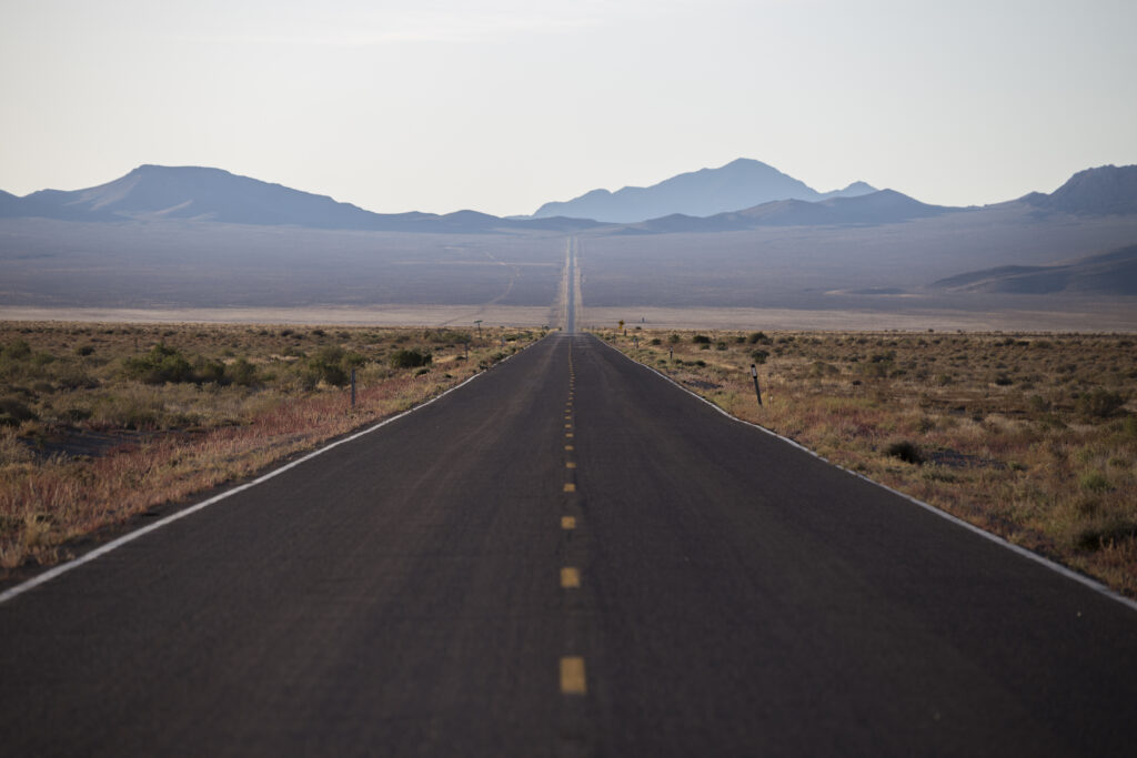 Long straight road across arid plain leading to distant blue mountains under clear sky wallpaper