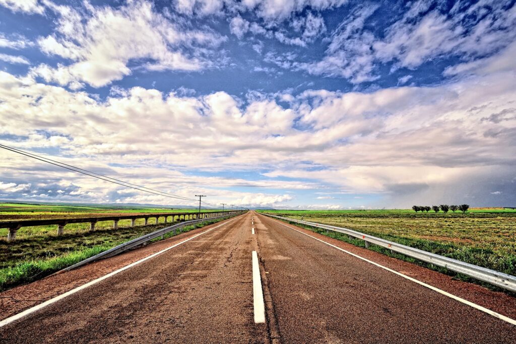 Straight road through green fields under dramatic cloudy sky vibrant landscape wallpaper background
