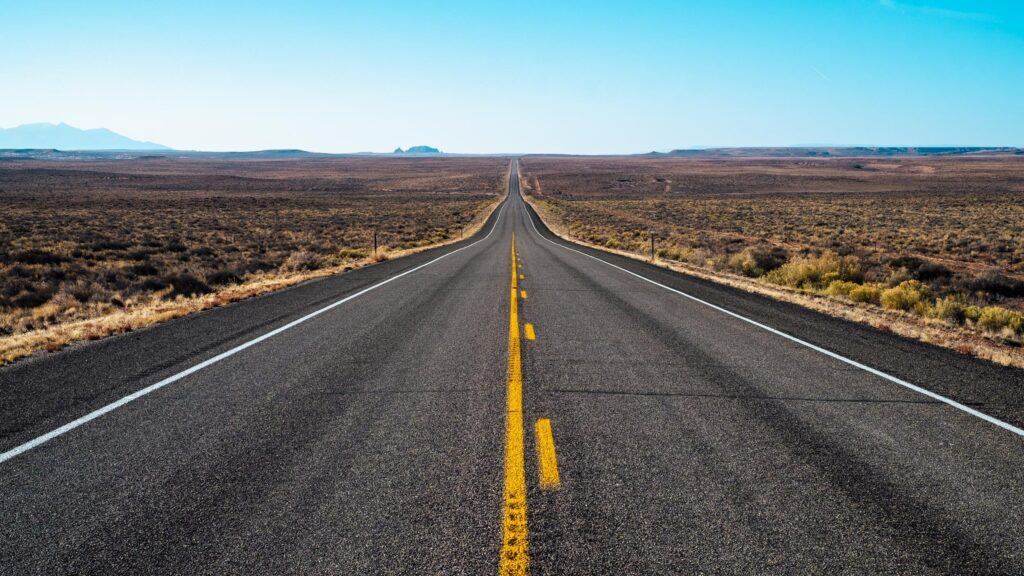 Straight road with yellow lines under blue sky leading to horizon symbolizing journey wallpaper