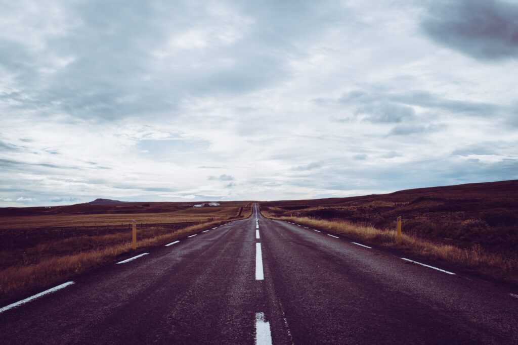 Long empty road with white markings under dramatic cloudy sky in serene rural landscape wallpaper