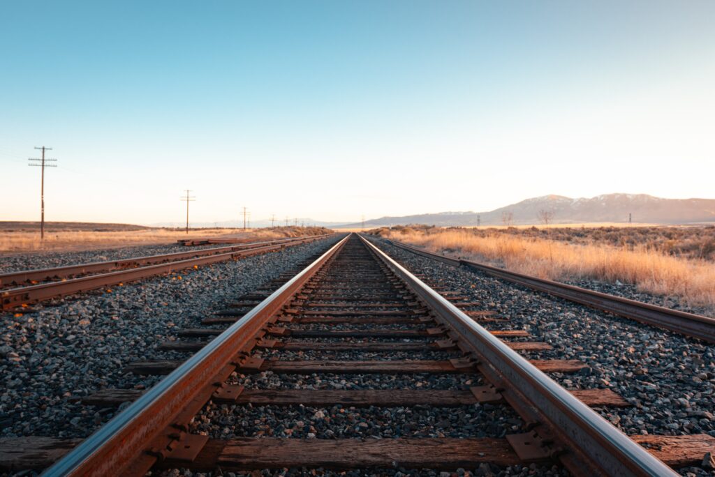 Parallel railway tracks under clear blue sky with warm sunlight on gravel and dry grass wallpaper