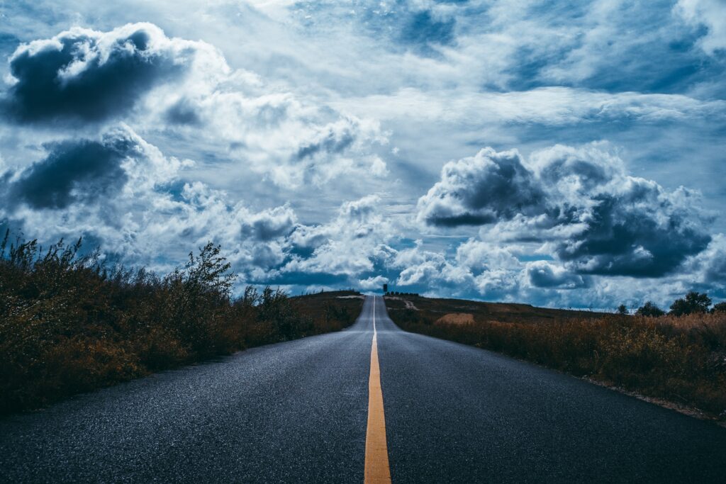 Empty road with vivid yellow lines under dramatic cloudy sky scenic wallpaper background
