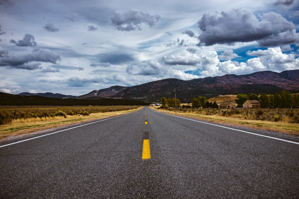 Straight road through fields and mountains under dramatic clouds inspiring travel adventure wallpaper