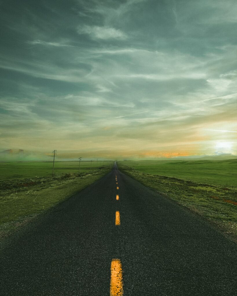 Long straight road with yellow lines through green fields at sunrise scenic travel wallpaper background