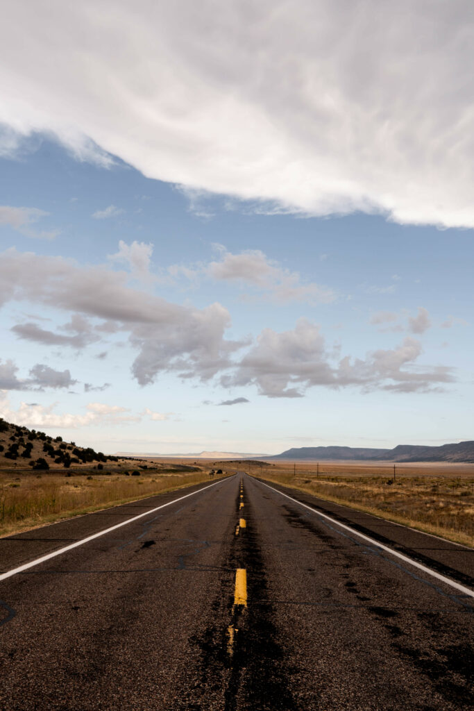 Long empty road with yellow lines through fields under dramatic cloudy sky wallpaper background