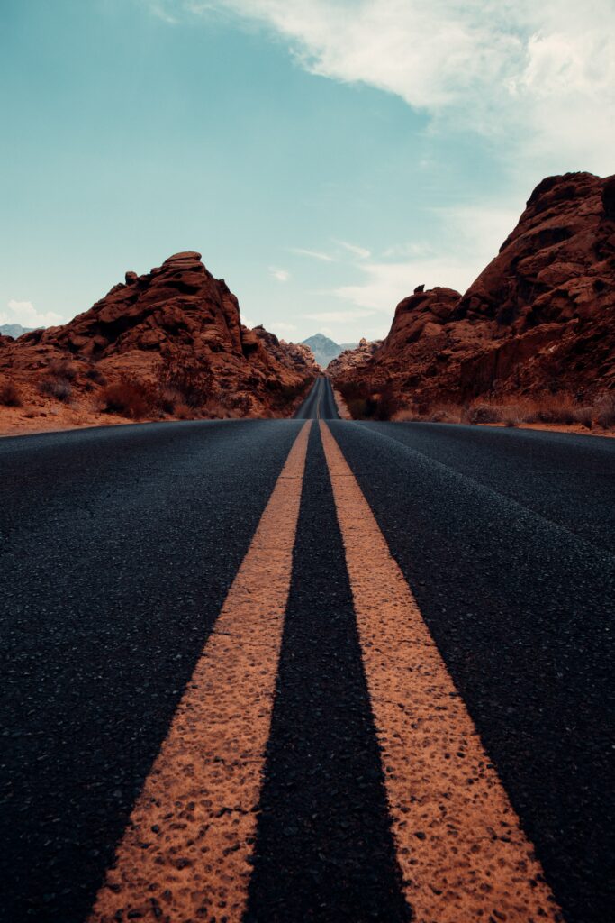Long straight road with yellow lines through red rock landscape under clear blue sky wallpaper