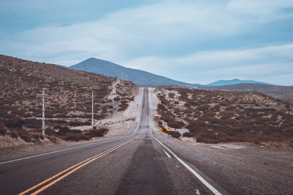 Straight road through rugged landscape leading to mountains under cloudy blue sky wallpaper