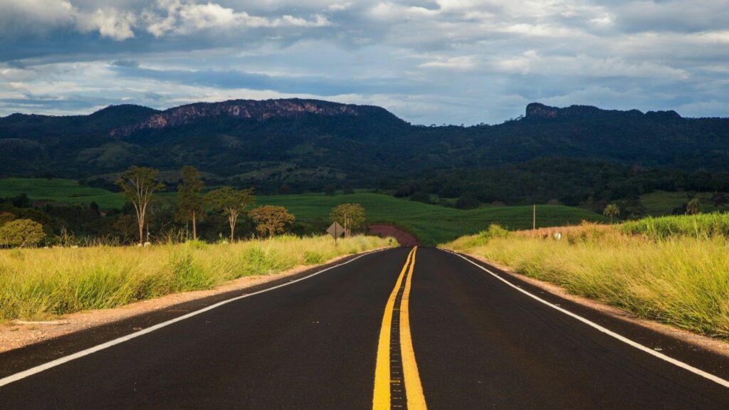 Smooth road with yellow lines through green fields and mountains under a vast sky wallpaper