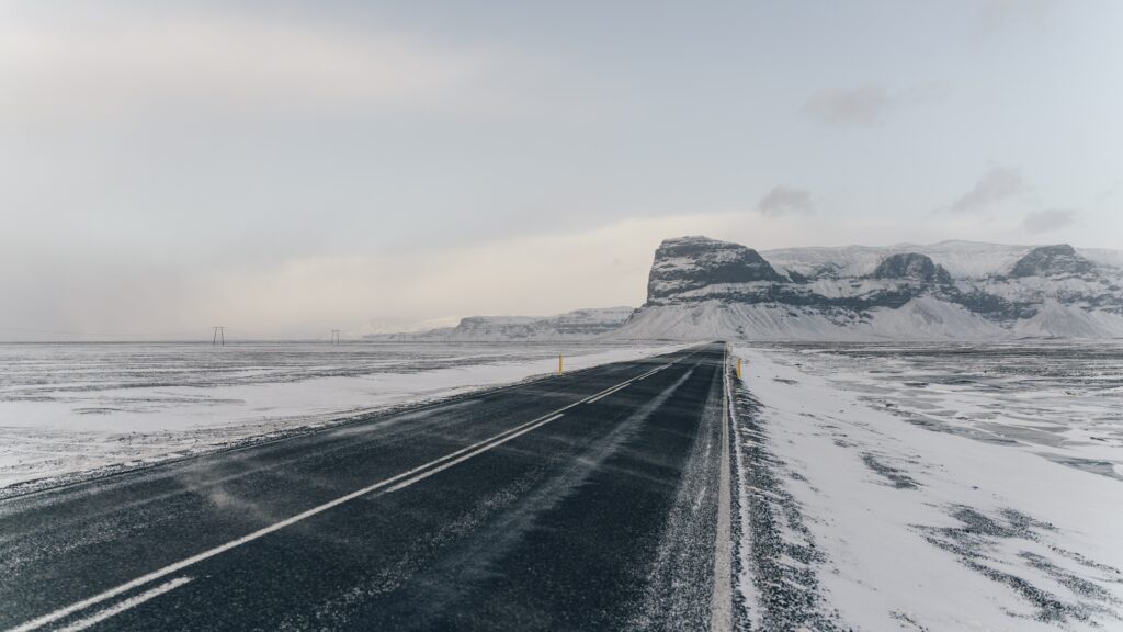 Empty winter road through snowy fields and distant mountains under a calm gray sky wallpaper background