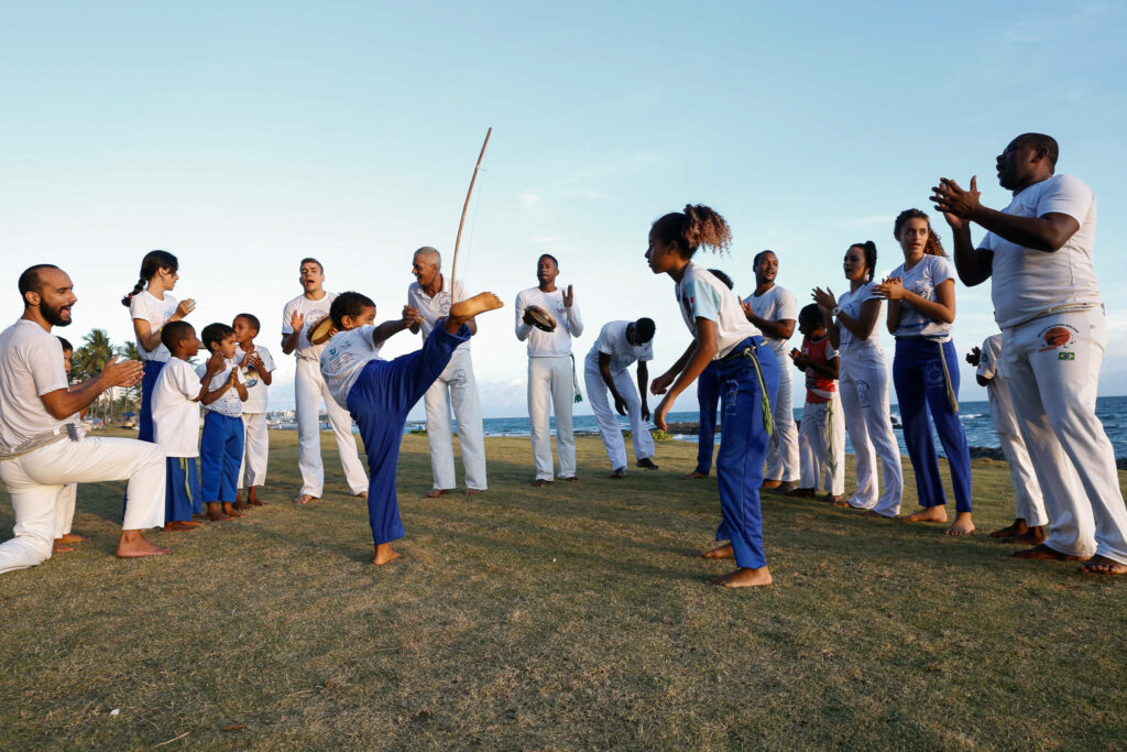 Joyful group practicing capoeira outdoors clapping and cheering young performer high kick Wallpaper