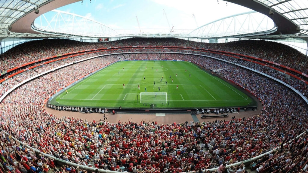 Vibrant football stadium wallpaper with red fans green pitch and dramatic lighting under arched roof