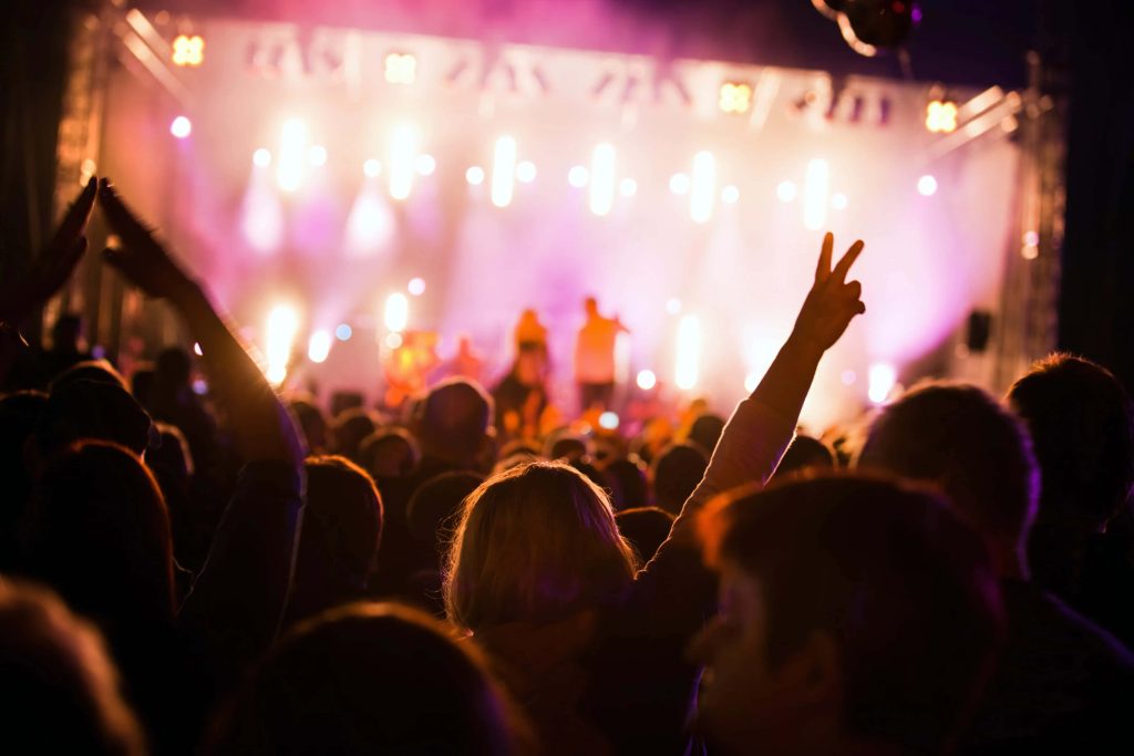 Energetic concert crowd with raised hands under vibrant purple and gold stage lights wallpaper