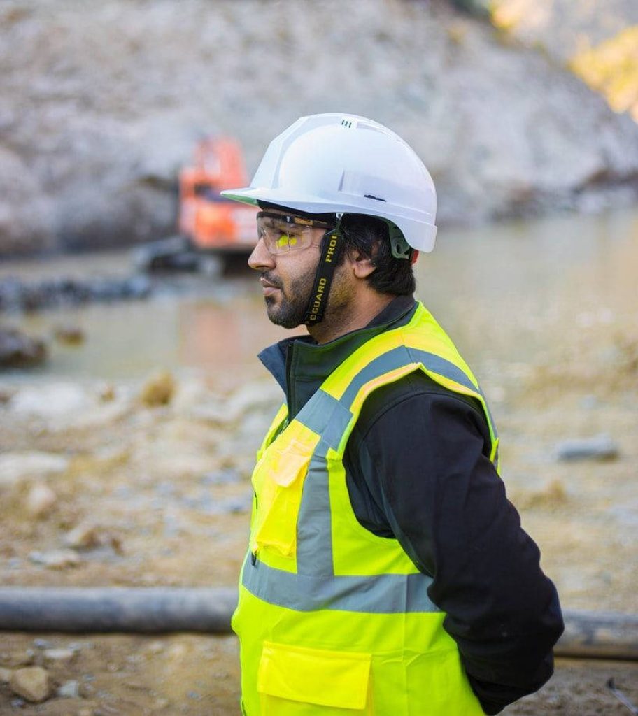 Engineer with hard hat and safety vest overseeing construction site with excavator background Wallpaper