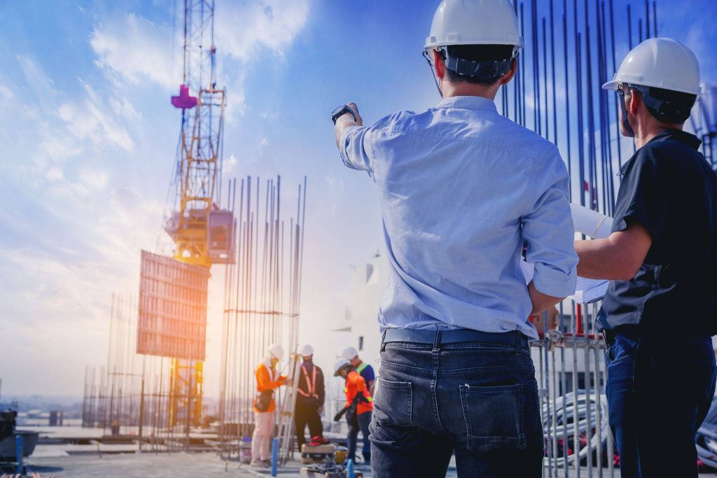 Two engineers in hard hats inspect construction site with crane and exposed rebar at sunset Wallpaper