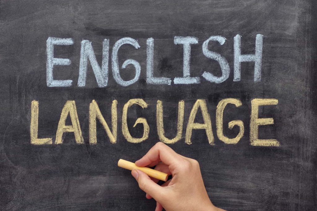 Hand holding yellow chalk writing English Language on black chalkboard educational wallpaper background