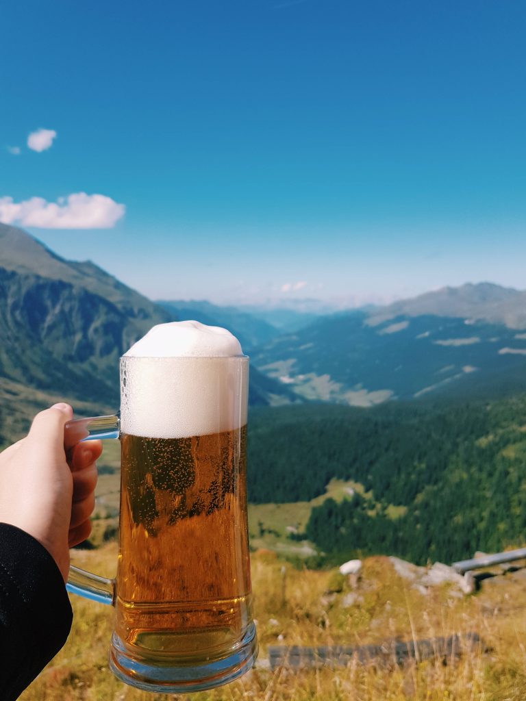 Refreshing golden beer mug held against bright green alpine mountain valley background wallpaper