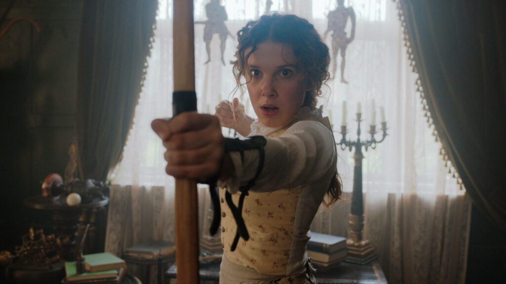 Enola Holmes practicing archery in Victorian room with antique decor and natural light wallpaper