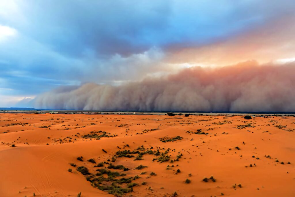 Enormous dust storm approaching golden sand dunes under dramatic sky in vast desert landscape Wallpaper