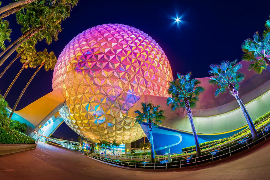 Epcot Globe glowing rainbow colors framed by palm trees night sky moon vibrant wallpaper background
