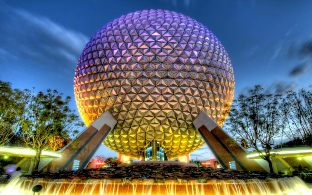 Epcot globe glowing gold and purple above fountain at twilight with trees and sky background Wallpaper