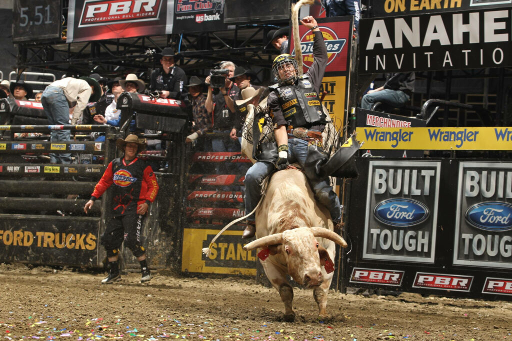 Bull rider grips tightly as powerful bull bucks in vibrant rodeo arena with energetic crowd Wallpaper