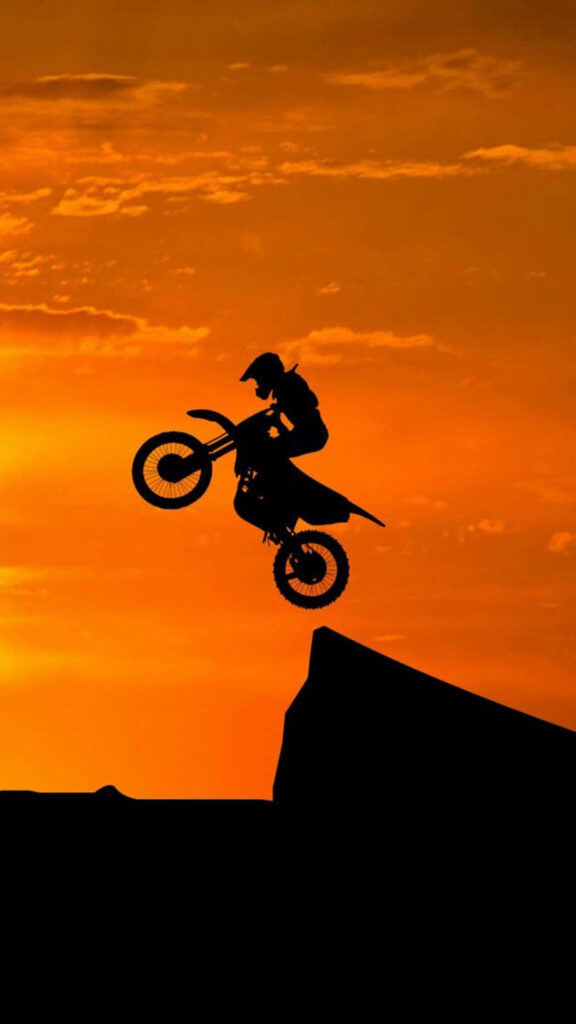 Dirt bike rider mid-air silhouette against vibrant orange sunset sky thrilling action wallpaper background