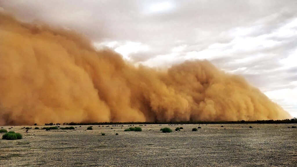 Massive dust storm over barren desert with swirling orange and brown skies under clouds Wallpaper