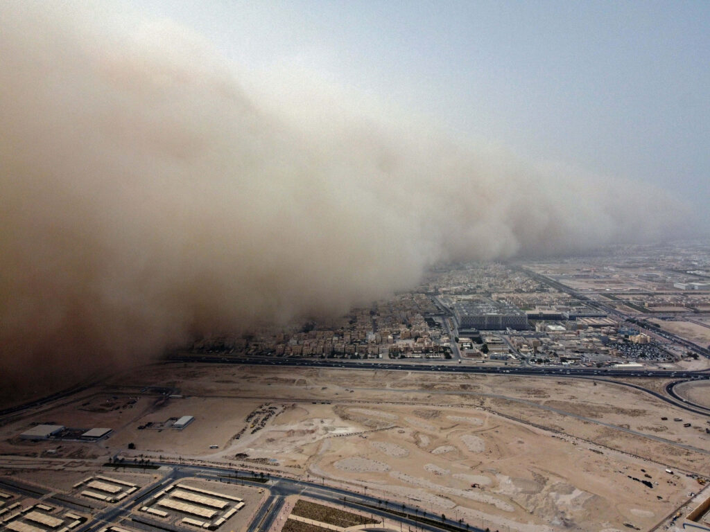 Massive dust storm engulfs city skyline casting golden haze over urban landscape background Wallpaper