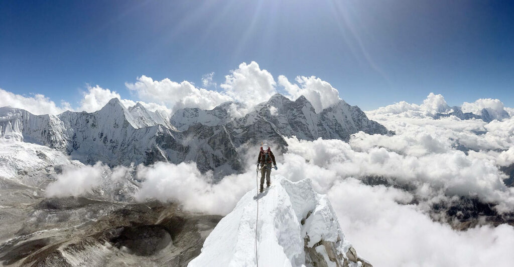 Climber stands on snowy mountain ridge with sunlit peaks and clouds majestic high altitude view Wallpaper