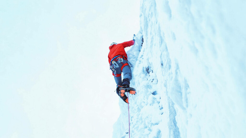 Climber in red jacket ascending steep icy wall surrounded by snowy frozen landscape wallpaper