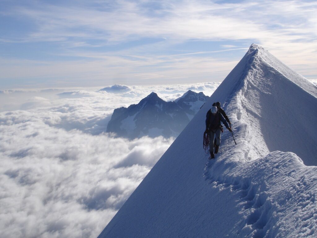 Climber ascending snowy sharp peak with vast clouds distant mountains snowy trail wallpaper background