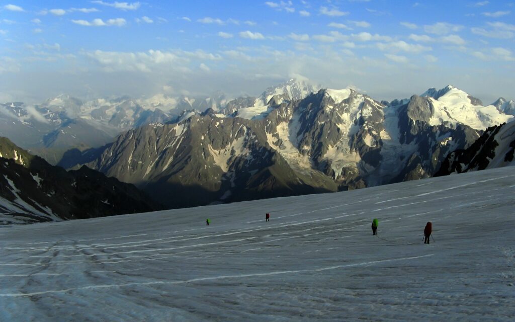 Climbers descending snowy slope with rugged mountains under bright blue sky high-altitude adventure Wallpaper