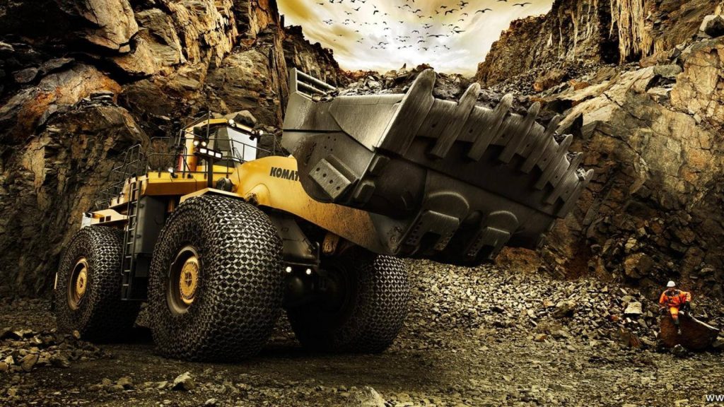 Yellow Komatsu wheel loader in rugged quarry with worker in high visibility gear background wallpaper