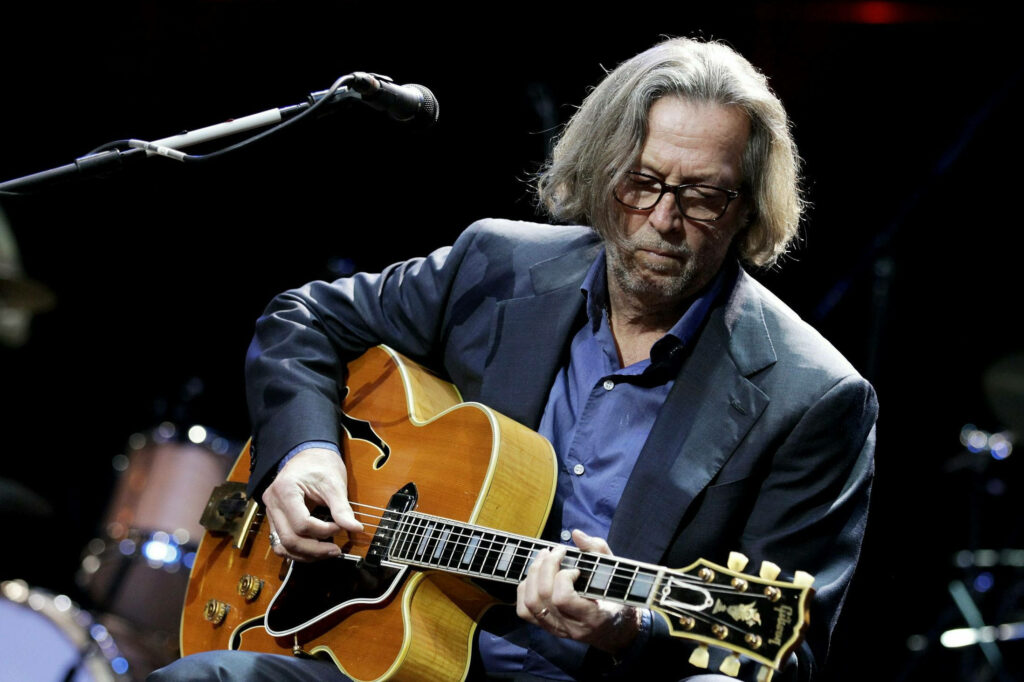 Eric Clapton playing acoustic guitar on stage focused passionate rock music wallpaper background