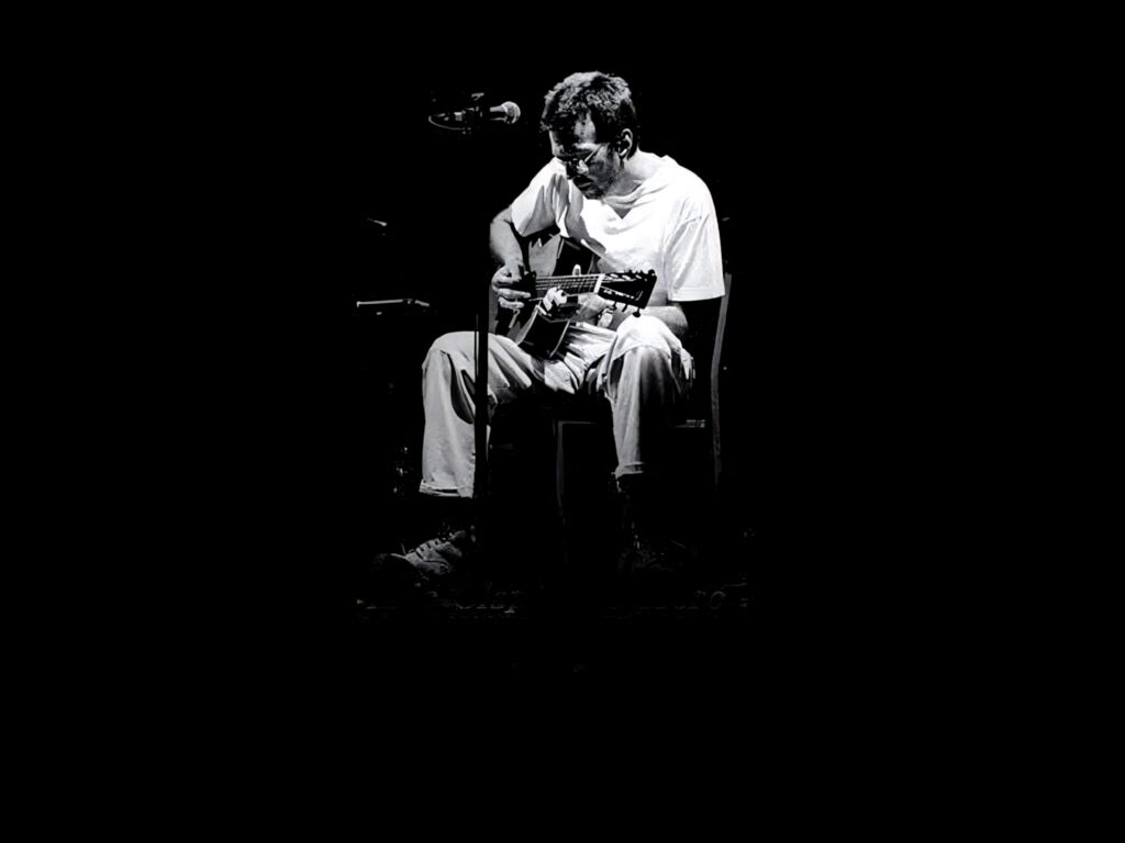 Eric Clapton playing acoustic guitar seated relaxed casual shirt dark background wallpaper